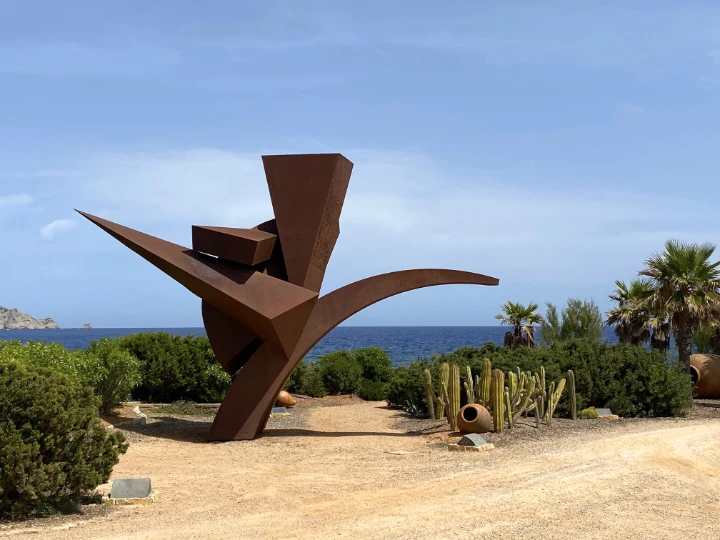 Abstrakte Cortenstahl-Skulptur an der Steilküste, im Hintergrund das Meer