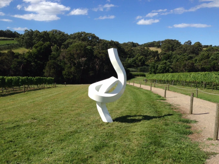 Weiße Bandskulptur auf einer Rasenfläche am Rand eines Weinbergs