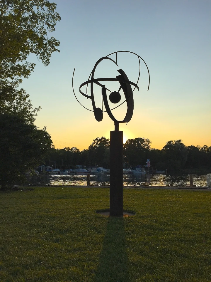 Kugelförmige Ringskulptur auf hohem Sockel als Silhouette vor Abendhimmel